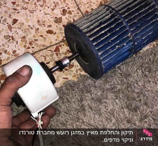 יד מחזיקה מנוע קטן ליד מאוורר של מזגן